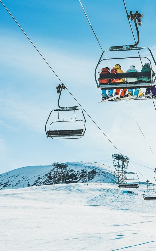 Skiers riding a chairlift above a snowy piste